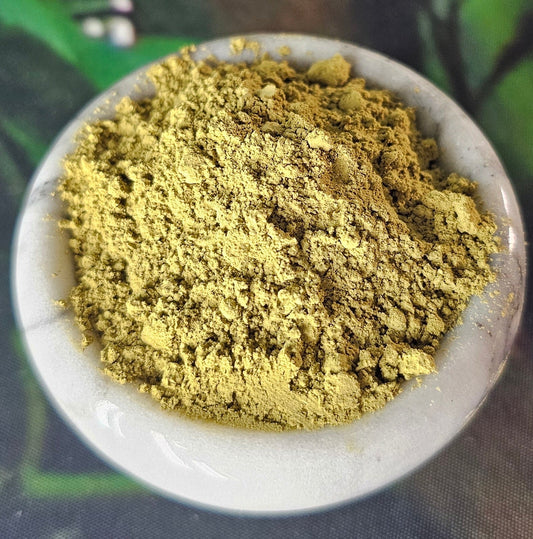 Fine gold kratom powder displayed in a modern small white marble dish with grey veining.